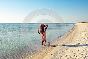 Traveler with funny dog goes along the deserted beach