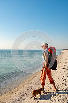 Traveler with funny dog stands on the deserted beach