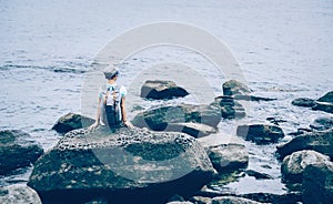 Traveler girl sitting on stone in the sea