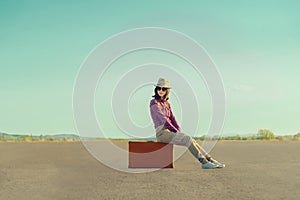 Traveler girl sitting on suitcase on road in summer