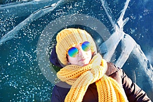A traveler girl in sunglasses is lying on the ice of the frozen Lake Baikal.