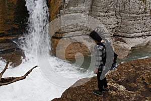 Traveler girl walking in waterfall canyon. Hiker girl with backpack standing near water of waterfall