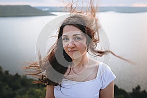 Traveler girl with windy hair relaxing on top of rock mountain, enjoying beautiful sunset view on river. Atmospheric moment. Copy