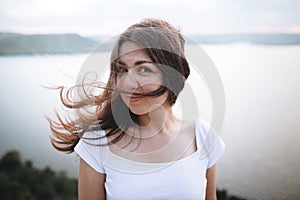 Traveler girl with windy hair relaxing on top of rock mountain, enjoying beautiful sunset view on river. Atmospheric moment. Copy