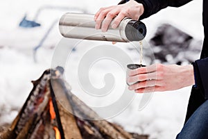 Traveler hands man Close-up pours tea from flasks into a cup in the forest near bonefire