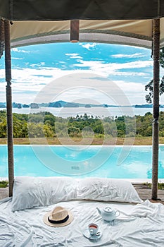 Traveler hat, hot tea cup and teapot on white bed against Beautiful ocean view background, Tourists relaxing in tropical resort