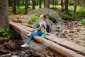 Traveler hiker with backpack crosses mountain river in Carpathian forest walking on bridge. Trip to summer Ukraine