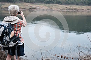 traveler hiker man with backpack hiking near lake. tourist backpacker use smart phone to take photo. travel lifestyle, summer vac