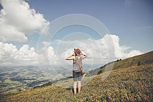 traveler hipster girl in hat, walking in sunny mountains, looking at clouds in sky. summer vacation. space for text. happy