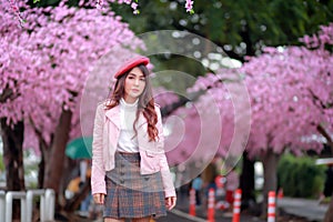 A traveler hipster woman sightseeing wear a red hat and a smooth leather dress with beautiful sakura cherry blossoms tree full