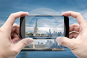 Traveler holding smartphone to take a photo of The Statue of Liberty