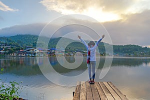 Traveler lifestyle woman feeling victorious facing on the bridge in the lake, season winter in the sunrise morning, relax and