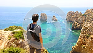 Traveler man with backpack enjoying and relaxing in front of stunning view in Southern Portugal. Back view of traveler male