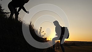 Traveler man holds out a woman`s hand to a traveler climbing to the top of the hill. Tourists climb the mountain at