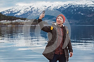 Traveler man taking self-portrait a photo with a smartphone. Tourist in a yellow backpack standing on a background of a