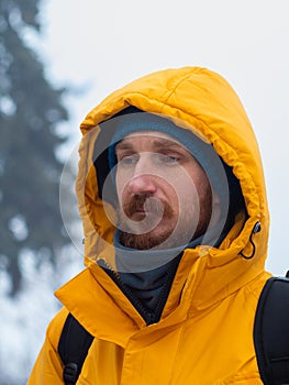 Traveler man in yellow coat with hood on blurred nature background. Authentic male tourist lifestyle portrait closeup