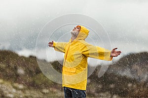 Man in yellow raincoat in the clouds mountains in stormy weather with rain