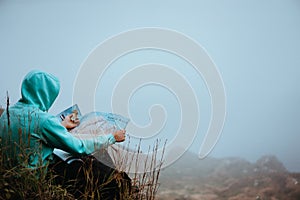 Traveler with a map sitting on the hill of a mountain in front of a gorgeous panorama view to the valley