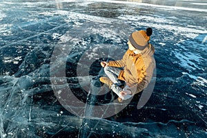 Traveler meditates sitting in Lotus position on pure ice of lake Baikal. Travel to beautiful places of nature