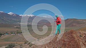 A traveler in the mountains climbs a rock relying on Swedish sticks