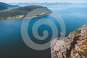 Traveler raised hands standing on cliff edge alone looking at aerial sea view