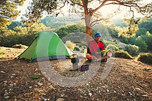 Traveler relaxes in the mountains among lush pines next to a burner