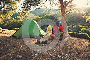 Traveler relaxes in the mountains among lush pines next to a burner