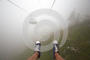 Traveler ride mountain cableway stretching down over beautiful early autumn mountain landscape in deep fog. First person