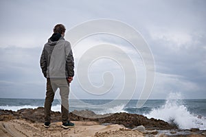 Traveler on the rocks near the sea looking far away at horizon. Rocky Atlantic Ocean Coastline and Stormy Weather