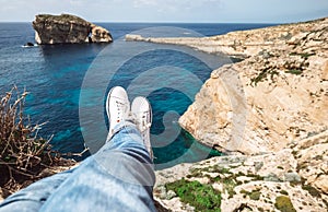 Traveler`s feet in white sneakers on the edge of rocky seaside