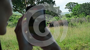 Traveler in safari hat and jumpsuit taking photo of rhinoceros in national park