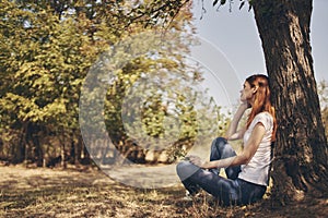 the traveler sits near a tree outdoors in the forest in jeans and a t-shirt