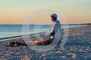 Traveler sits next to a bonfire on the seashore