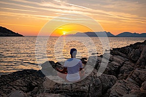 Traveler sits on the rock seashore and practicing yoga