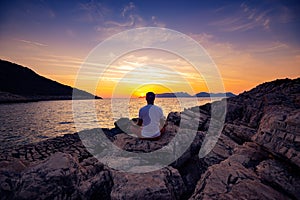 Traveler sits on the rock seashore and practicing yoga