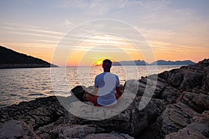 Traveler sits on the rock seashore and practicing yoga