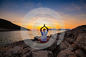 Traveler sits on the rock seashore and practicing yoga during sunset
