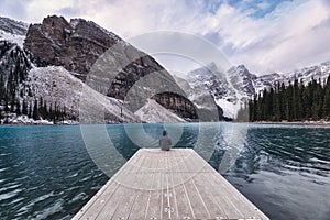 Traveler sitting on wooden pier with rocky mountain in Moraine lake at Banff national park