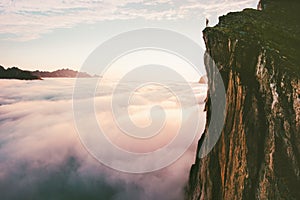 Traveler standing on cliff edge mountain top above sunset clouds