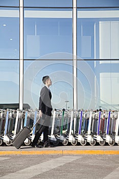 Traveler with suitcase next to row of luggage carts at airport