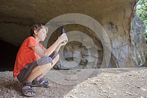 Traveler taking photo of rocky landscape with camera phone from mountain cave