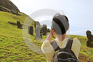 Traveler taking pictures of abandoned massive Moai statues scattered on Rano Raraku volcano, former Moai quarry on Easter Island
