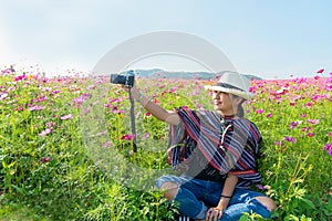 Traveler or tourism Asian women sitting and holding camera take a photo in the cosmos flower field in vacations time.  People smil