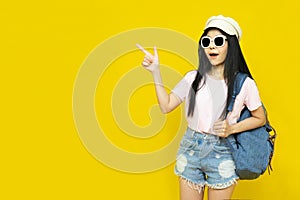 Traveler tourist beautiful young asian woman in casual clothes,cap and sunglasses with backpack isolated on yellow background.