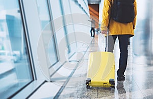 Traveler tourist in bright jacket with yellow suitcase backpack at airport on background large window blue sky, man waiting