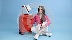 Traveler tourist woman in casual clothes and white hat holding money with passport, sitting at the suitcase