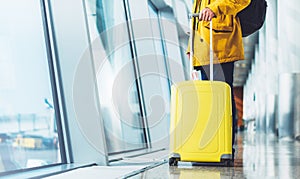 Traveler tourist with yellow suitcase backpack at airport on background large window blue sky, man in bright jacket waiting