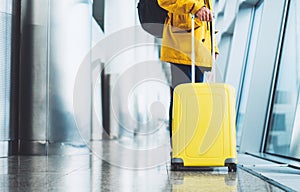 Traveler tourist with yellow suitcase backpack at airport on background large window, man in bright jacket waiting in departure