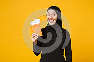 Traveler tourist young arabian muslim woman in hijab black clothes hold passport tickets isolated on yellow wall