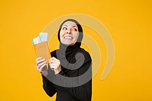 Traveler tourist young arabian muslim woman in hijab black clothes hold passport tickets isolated on yellow wall